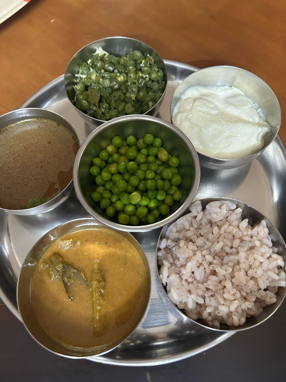 Traditional South Indian thali with hand-pounded red rice, dal, beans poriyal, peas, yoghurt, and sambar with okra
